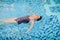 Beautiful adult woman in striped swimsuit swimming in blue pool on her back at resort. Sport activity health concept.