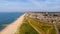 A beautiful aerial  seaside view with sandy beach, crystal blue water, groynes breakwaters and green vegetation dunes along a