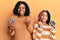 Beautiful african american mother and daughter holding donuts screaming proud, celebrating victory and success very excited with