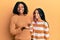 Beautiful african american mother and daughter wearing wool winter sweater amazed and smiling to the camera while presenting with