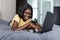 Beautiful african american professional woman laying relaxing on hotel bed, using a laptop computer, reading serene, travel