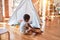 Beautiful african american toddler putting on shoes outside tipi at kindergarten