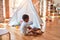 Beautiful african american toddler putting on shoes outside tipi at kindergarten