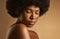 Beautiful african american woman with afro hair and glowing radiant skin posing against a brown studio background. Young