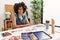 Beautiful african american woman with afro hair painting at art studio smiling looking to the side and staring away thinking