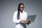 Beautiful African American woman doctor or nurse holding a laptop computer isolated on a gray background