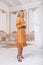 Beautiful african mixed young woman in fashionable dress and heels posing near crystal chandelier in luxury interior.