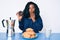 Beautiful african woman eating breakfast holding cholate donut covering mouth with hand, shocked and afraid for mistake