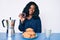 Beautiful african woman eating breakfast holding cholate donut looking positive and happy standing and smiling with a confident