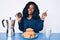 Beautiful african woman eating breakfast holding cholate donut smiling happy pointing with hand and finger to the side