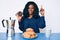 Beautiful african woman eating breakfast holding cholate donut smiling with an idea or question pointing finger with happy face,