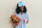 Beautiful african young woman wearing pajama, holding teddy bear and drinking coffee clueless and confused expression