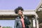 Beautiful afro haired woman with black jacket and black headphones around her neck smiles looking aside while taking a walk