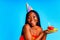 beautiful afro woman with georgeus makeup wear birthday hat and hold cake in blue studio
