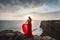 This beautiful AI generated girl in a red dress meditates on a cliff edge against the backdrop of a velocleptic, summer sea