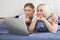 Beautiful amorous couple using laptop, on bed. Beautiful woman and handsome man read the news on internet. Concept