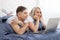 Beautiful amorous couple using laptop, on bed. Beautiful woman and handsome man read the news on internet. Concept