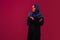 Beautiful arab woman posing in stylish hijab isolated on burgundy studio background in neon light. Fashion, beauty