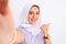 Beautiful arabian girl wearing hijab make selfie by camera over isolated white background pointing and showing with thumb up to