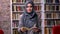 Beautiful arabic woman in grey hijab are standing still and holding book, serious confident galce at camera, library