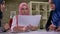 Beautiful arabic woman in pink hijab is having work conversation with other muslim females holding documents, sitting at