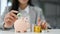 Beautiful Asian businesswoman insert coins in a pin piggy bank on the table. saving money