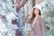 Beautiful Asian female wears a white hat and plaid coat while looking at the camera and stands outdoors near Christmas tree coated