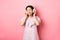 Beautiful asian girl close eyes while listening music in headphones, enjoying soft sound, standing against pink