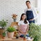 Beautiful Asian girl man ware jean and pink apron sit and stand together looking at camera in white room surround by trees