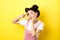 Beautiful asian girl showing v-sign and pouting cute, making silly face with makeup, standing on yellow background