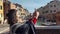 Beautiful asian girl tourist in red sweater enter in frame taking photo of the picturesque venetian canal with her