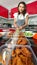 Beautiful Asian housewife and shop owner wearing apron preparing Thai style food,  fried fish-paste patty, for sale and ready to