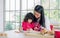 Beautiful Asian mother and mixed race adorable little daughter sitting in kitchen, drawing, painting, doing homework or activities