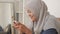 Beautiful Asian muslim woman using phone while relaxing on sofa, playing games or watching streaming online video