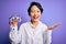 Beautiful asian optical girl wearing coat holding optometry glasses over purple background very happy and excited, winner