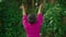 A beautiful Asian woman does a dancing ritual while wearing a pink dress and makeup in front of the big tree full of green bushes