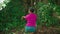 A beautiful Asian woman does a dancing ritual while wearing a pink dress and makeup in front of the big tree full of green bushes