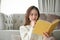 Beautiful Asian woman in the living room enjoying reading a book or adventure fiction novel