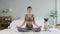 Beautiful Asian woman practice yoga lotus pose with dog pug breed enjoy and relax with yoga in bedroom at home