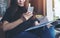 A beautiful Asian woman with smiley face using and looking at smart phone while holding magazine in modern cafe