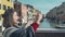 Beautiful asian woman tourist in red sweater enter in frame taking photo of the picturesque venetian canal with her