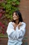 Beautiful Asian young woman standing in a knitted purple warm cardigan by a brick wall