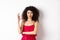 Beautiful assertive woman with curly hairstyle and makeup, wearing red dress, showing okay sign and smiling in approval