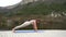 A beautiful, athletic middle-aged woman in a beige suit is stretching, doing push-ups. Lake, river, mountains and forest