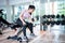 Beautiful athletic muscular Asian woman pumps up the muscles by one arm lifts dumbbell exercise on bench in fitness gym