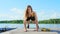 Beautiful, athletic young blond woman stretching, doing different exercises, jumping, lunges, squats. Lake, river, blue