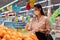 Beautiful attractive asian woman wearing medical face mask and rubber gloves choosing orange on fruits shelf in supermarket.Young