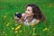 Beautiful, attractive girl-photographer with curly hair holds a camera and lying on the grass with blooming dandelions