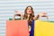 Beautiful, attractive young lady with funny facial expression stretches shopping bags to camera. Close studio portrait