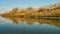 Beautiful autumn hillside covered in orange and yellow bushes and their reflection in the blue river